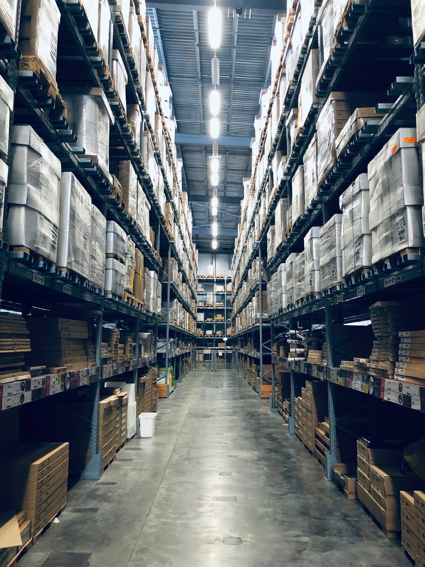 Pasillo de una bodega entre estanterías altas cargadas de pallets, con la perspectiva perdiéndose al fondo.