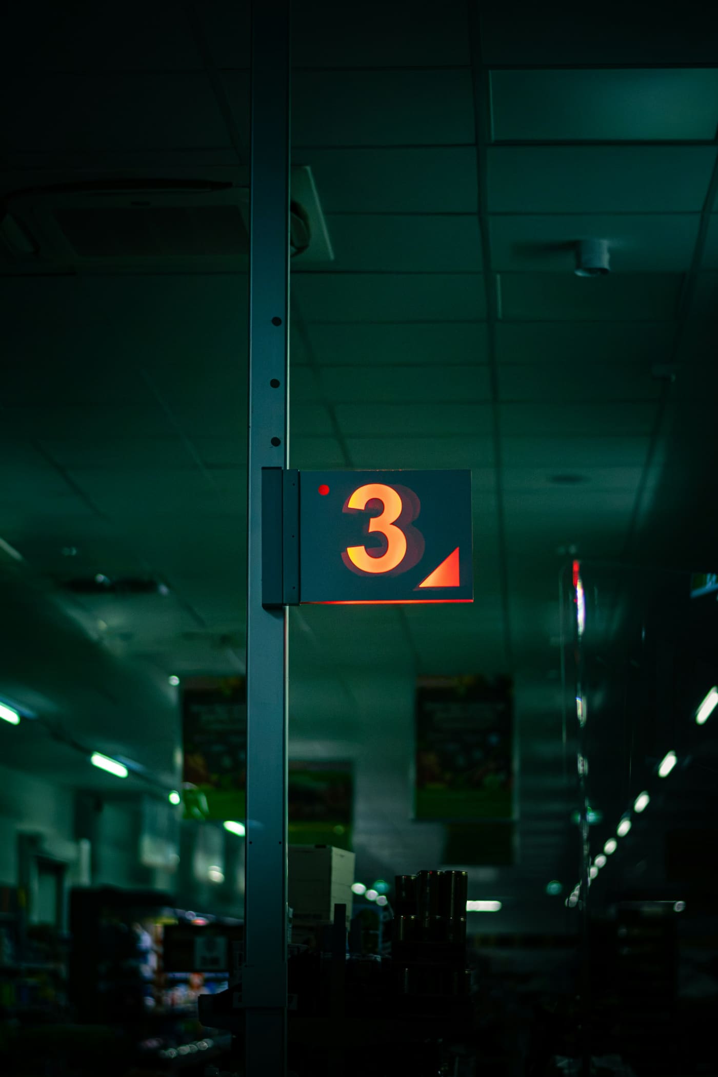 Interior de un autoservicio en penumbra, con góndolas de producto y un rótulo iluminado al fondo del pasillo.